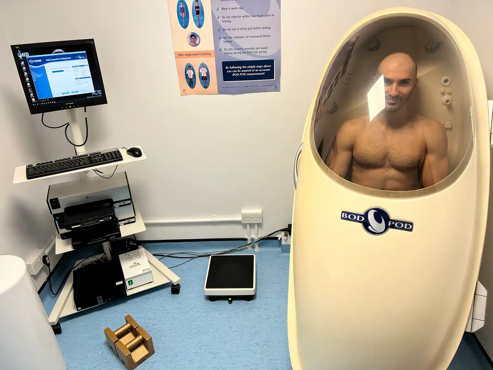 Dr Stefan Kolimechkov inside a Bod Pod body-composition assessment chamber with its measurement workstation visible.