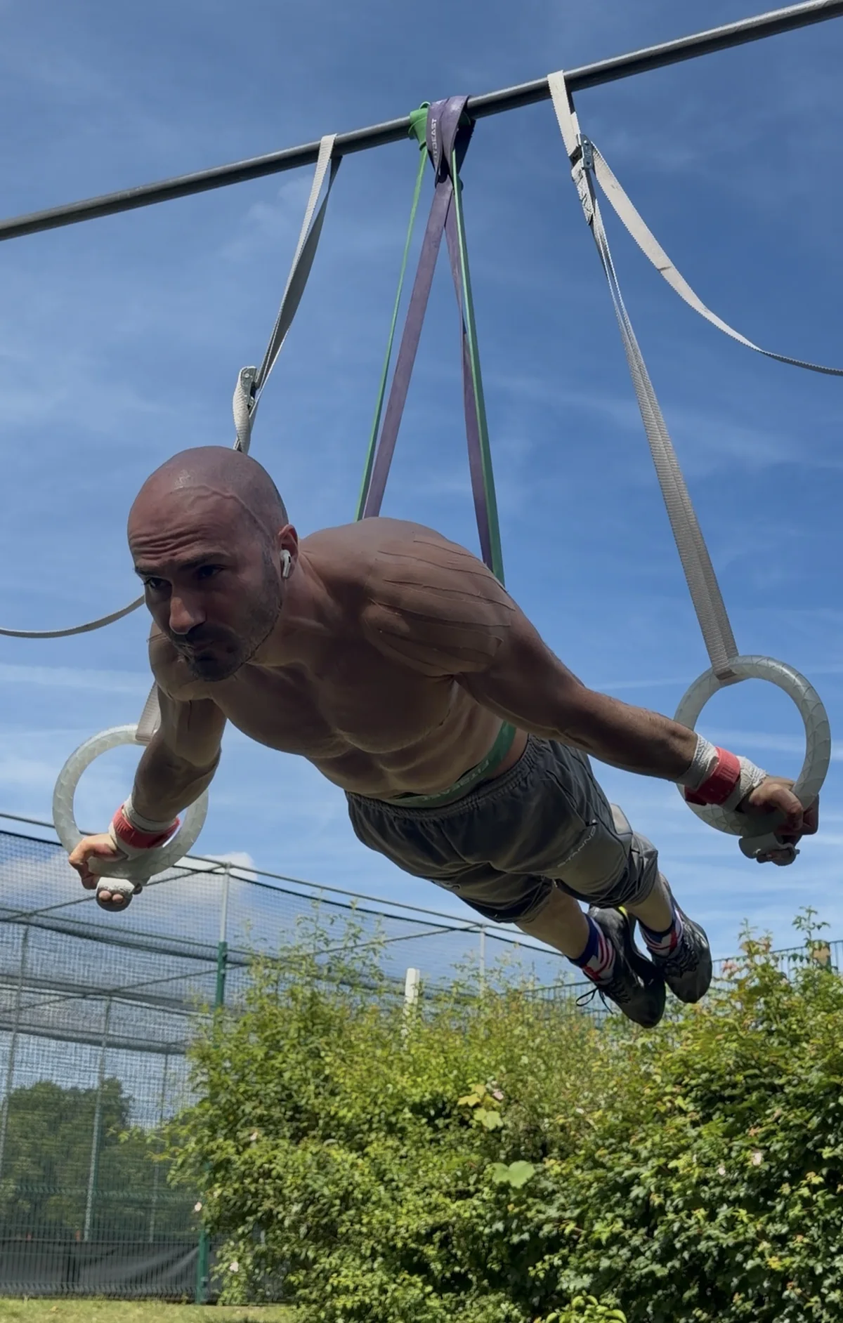 Stefan Kolimechkov practising Maltese strength training on outdoor rings with elastic-band assistance in Holland Park.